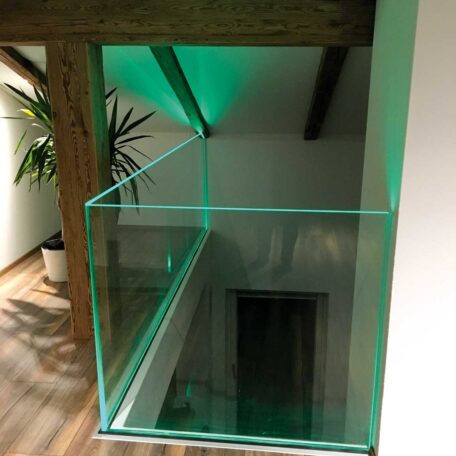 Glasgeländer an einer Galerie mit grünem Licht, Holzbalken und Zimmerpflanze. HANSEL.kraus metalltechnik gmbh