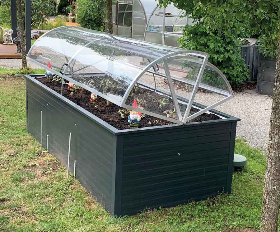 Hochbeet mit transparenter Abdeckung, darin wachsen verschiedene Jungpflanzen im Garten. de HANSEL.kraus metalltechnik gmbh