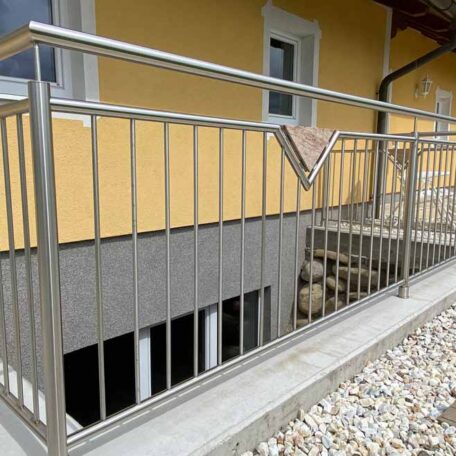 Edelstahlgeländer mit modernem Design vor gelber Hauswand, Innenhof mit Steinen. HANSEL.kraus metalltechnik gmbh