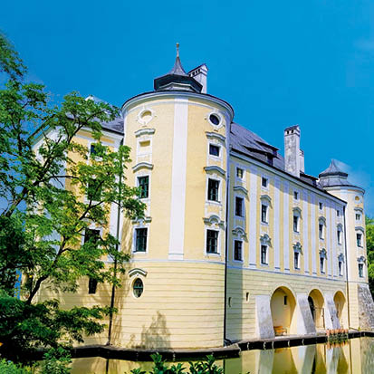 Schloss mit gelber Fassade und Rundtürmen spiegelt sich im Wasser unter blauem Himmel. de HANSEL.kraus metalltechnik gmbh