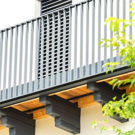 Moderner Balkon mit dunklem Geländer und Holzbalken, daneben grüner Baumast. HANSEL.kraus metalltechnik gmbh