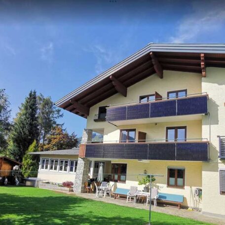 Modernes Wohnhaus mit großzügigem Garten, Sonnenterrasse und Solarpaneelen am Balkon bei blauem Himmel. HANSEL.kraus metalltechnik gmbh