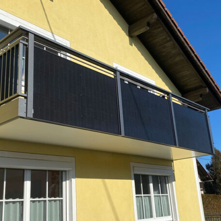 Moderner Balkon mit dunkler Verkleidung an gelber Hausfassade, blauer Himmel im Hintergrund. de HANSEL.kraus metalltechnik gmbh