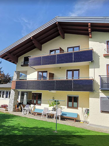 Wohnhaus mit Photovoltaik-Modulen an Balkonen, sonniger Garten, blauer Himmel. HANSEL.kraus metalltechnik gmbh