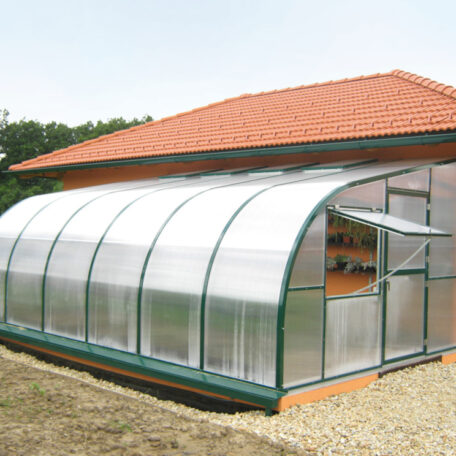 Gewächshaus mit gebogenem Dach und Fenstern steht neben Haus mit rotem Ziegeldach. HANSEL.kraus metalltechnik gmbh