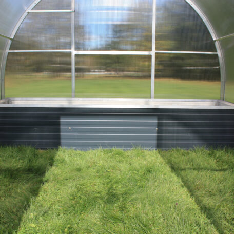 Innenraum eines leeren, modernen Gewächshauses mit Rasenboden und transparenter Kunststoffabdeckung. de HANSEL.kraus metalltechnik gmbh