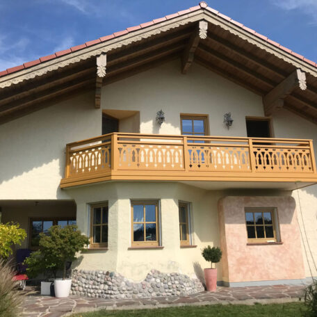 Zweistöckiges Einfamilienhaus mit Holzbalkon, Satteldach und gepflegtem Garten im Vordergrund. de HANSEL.kraus metalltechnik gmbh