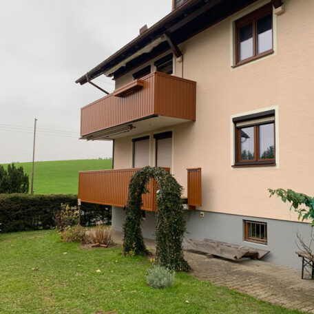 Wohnhaus mit zwei braunen Balkonen, gepflegtem Garten und Blick auf grüne Wiese. HANSEL.kraus metalltechnik gmbh