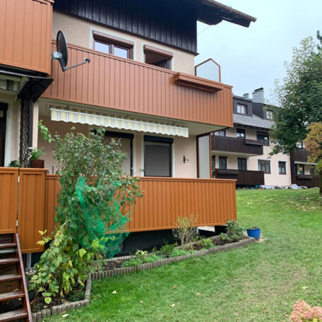 Mehrfamilienhaus mit hölzernen Balkonen, Gartenbereich und weiteren Wohngebäuden im Hintergrund. HANSEL.kraus metalltechnik gmbh