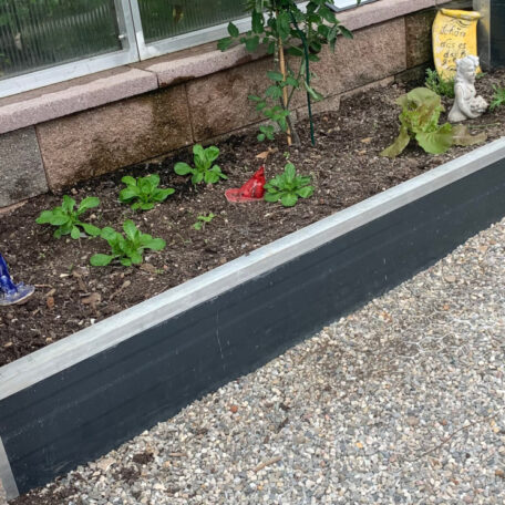 Ein bepflanztes Beet mit Gartendekorationen an einem Hausfenster und Kiesweg davor. de HANSEL.kraus metalltechnik gmbh
