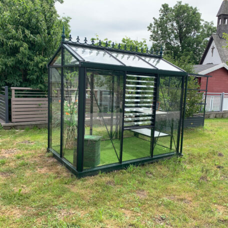 Gewächshaus aus Glas mit Regalen und Tisch steht auf einer Wiese im Garten. HANSEL.kraus metalltechnik gmbh
