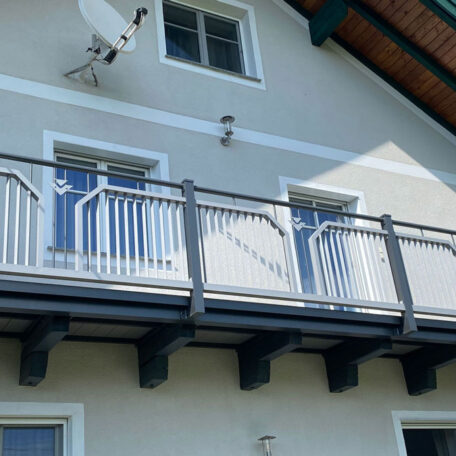 Zwei Fenster und moderner Balkon an einem hellen Einfamilienhaus, blaue Details sichtbar. HANSEL.kraus metalltechnik gmbh