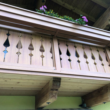 Holzbalkon mit dekorativen Schnitzereien und Blumenkasten mit lila Blüten, traditionelle Bauweise. HANSEL.kraus metalltechnik gmbh