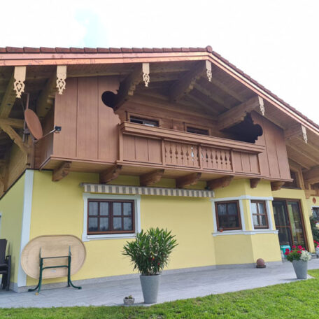 Traditionelles gelbes Haus mit Holz-Balkon und Terrasse, davor Topfpflanzen im grünen Garten. HANSEL.kraus metalltechnik gmbh