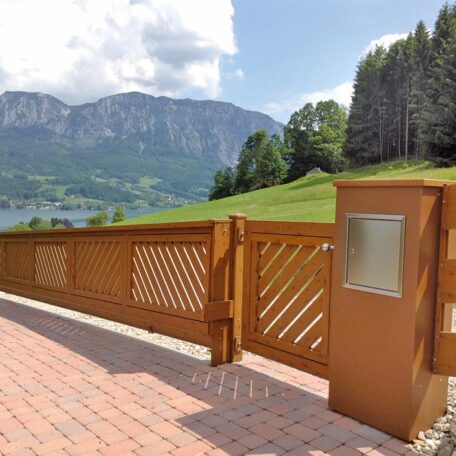 Braunes Gartentor mit gemauertem Sockel vor Berglandschaft und grüner Wiese, sonniger Tag. HANSEL.kraus metalltechnik gmbh