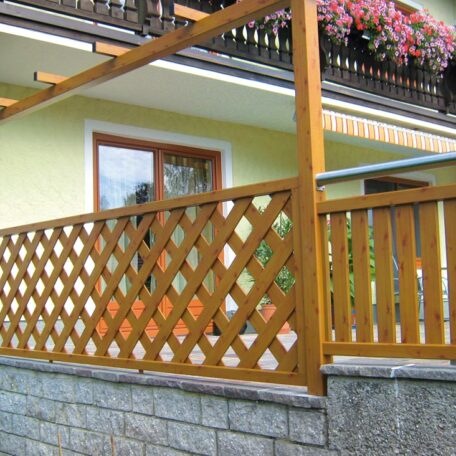 Holzgeländer mit Rankgitter und Blumen am Balkon vor gelbem Haus auf Steinmauer. de HANSEL.kraus metalltechnik gmbh