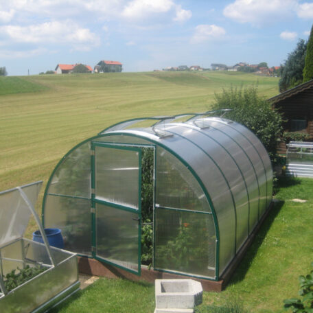 Gewächshaus im Garten vor Wiesen und Feldern bei sonnigem Wetter, ländliche Umgebung. HANSEL.kraus metalltechnik gmbh