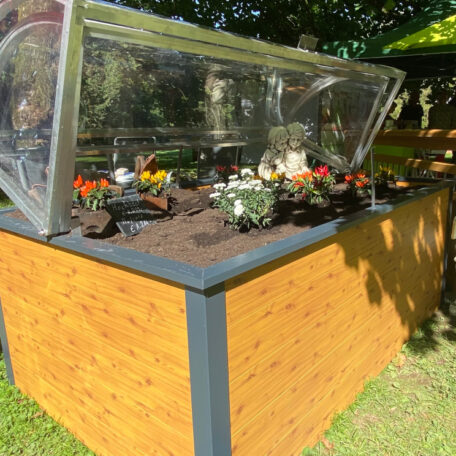 Hochbeet mit durchsichtiger Abdeckung, bepflanzt mit bunten Blumen, im sonnigen Garten. de HANSEL.kraus metalltechnik gmbh