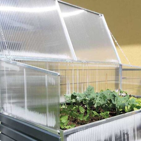 Hochbeet mit geöffnetem, transparentem Frühbeet-Aufsatz, darin wachsen grüne Gemüsepflanzen. de HANSEL.kraus metalltechnik gmbh