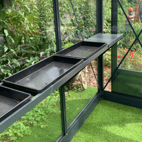 Schwarzes Regal mit Anzuchtschalen im Gewächshaus vor grünem Pflanzenhintergrund, geeignet für Urban Gardening. HANSEL.kraus metalltechnik gmbh