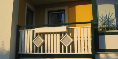 Balkon mit gelber Wand, weißem Geländer und zwei quadratischen Deko-Elementen, sonnige Beleuchtung. HANSEL.kraus metalltechnik gmbh