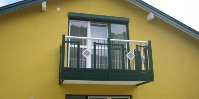 Obergeschoss eines gelben Hauses mit grünem Balkon und weißen Fenstertüren, Tageslicht. HANSEL.kraus metalltechnik gmbh