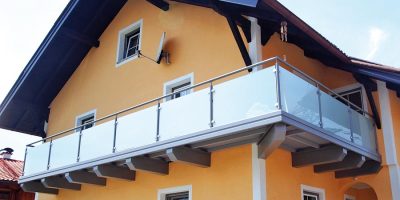 Gelbes Einfamilienhaus mit großzügigem Balkon und moderner Glasbrüstung unter blauem Dach. HANSEL.kraus metalltechnik gmbh