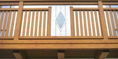Holzbalkon mit senkrechten Streben und rautenförmigem Glaselement an weißer Hausfassade. HANSEL.kraus metalltechnik gmbh