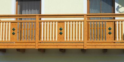 Holzbalkon mit senkrechten Streben und zwei grünen Rauten vor hellgelber Hauswand. HANSEL.kraus metalltechnik gmbh