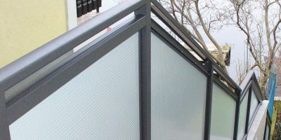 Treppengeländer mit Milchglasfüllung und Metallrahmen neben Haus, Bäume im Hintergrund. HANSEL.kraus metalltechnik gmbh