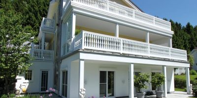 Modernes weißes Mehrfamilienhaus mit großzügigen Balkonen und Garten vor bewaldeter Kulisse. HANSEL.kraus metalltechnik gmbh
