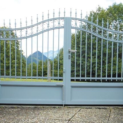 Zweigeteiltes Metalltor mit spitzen Ornamenten vor einer grünen Landschaft mit Bergen im Hintergrund. HANSEL.kraus metalltechnik gmbh