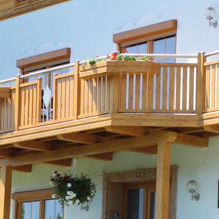 Holzbalkon mit Blumenkasten und hängendem Pflanzgefäß an einem hellen Haus. HANSEL.kraus metalltechnik gmbh