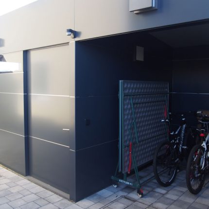 Zwei Fahrräder stehen unter einem modernen Carport neben einem Gitter, gepflasterter Boden. HANSEL.kraus metalltechnik gmbh