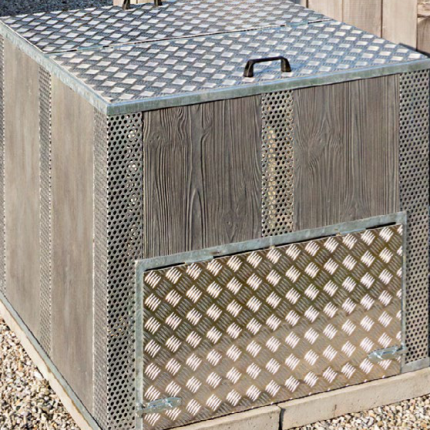 Holzverkleidete Mülltonnenbox mit Gittereinsatz steht außen auf Kiesfläche. de HANSEL.kraus metalltechnik gmbh